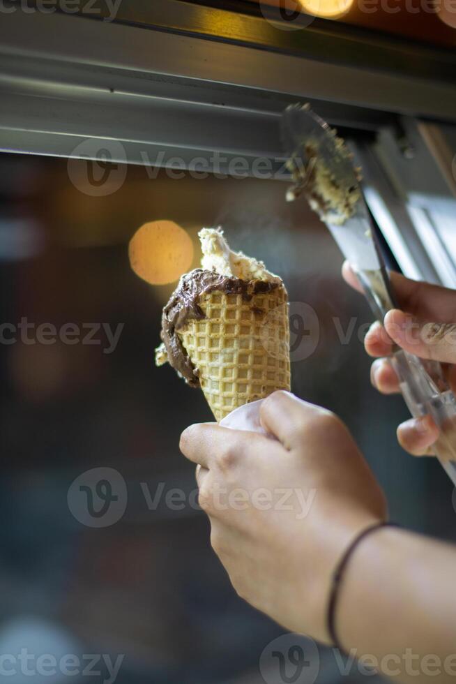 Close up hand of a person scooping ice cream in to a cone with blurred background photo