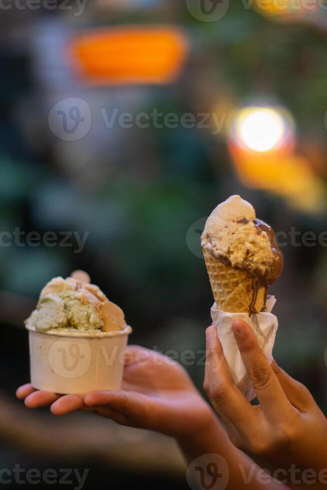 Close up hand of a person holding a cup and a cone of ice cream with blurred background photo