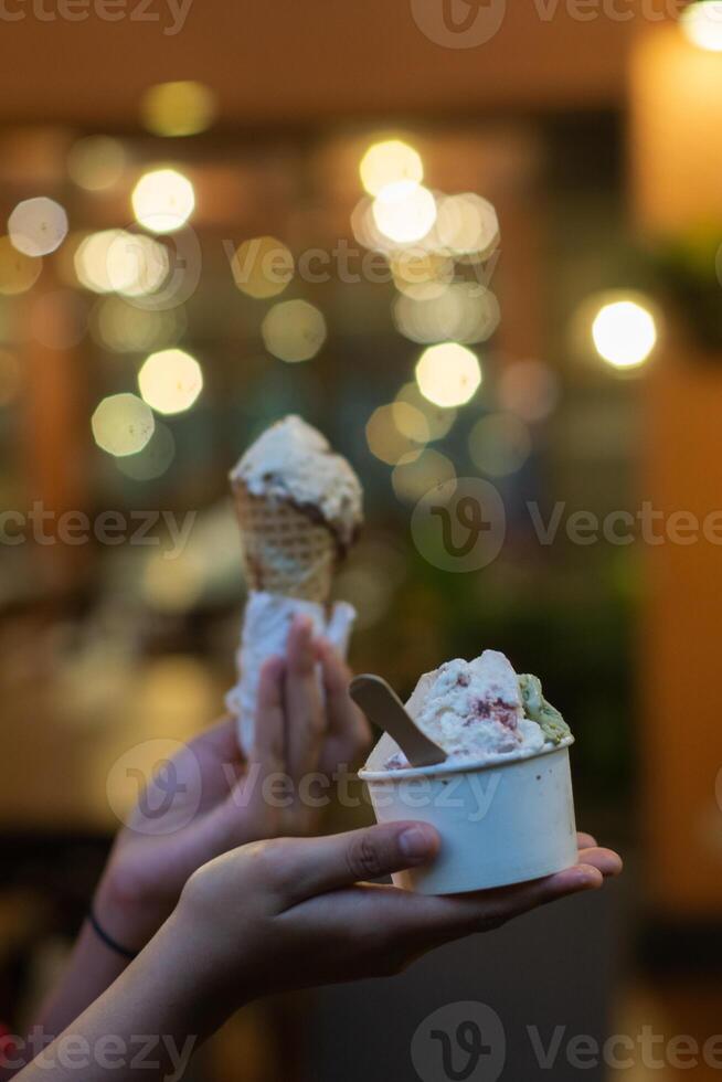 Close up hand of a person holding a cup and a cone of ice cream with blurred background photo