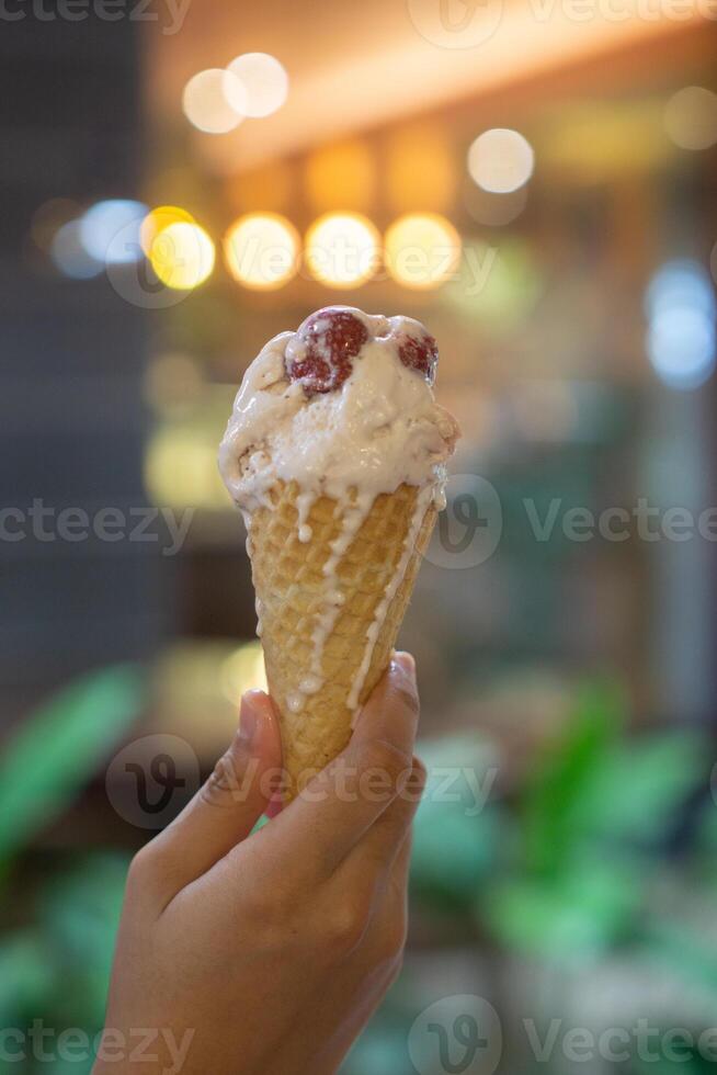 Close up hand of a person holding a cone of ice cream with blurred background photo