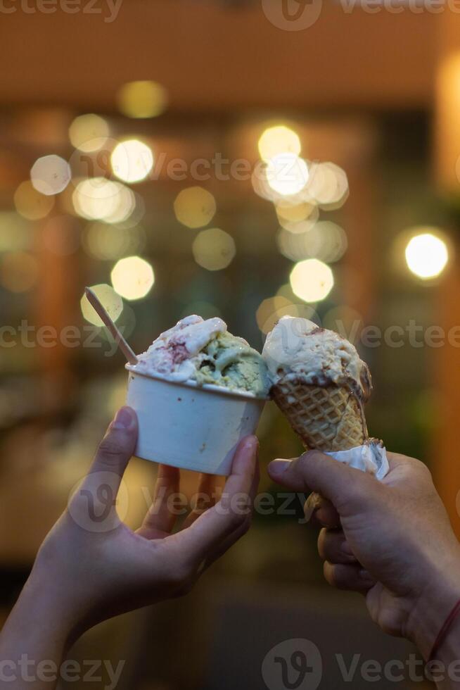 Close up hand of a person holding a cup and a cone of ice cream with blurred background photo