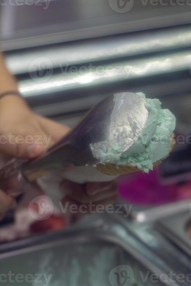 Close up hand of a person scooping ice cream in to a cone with blurred background photo