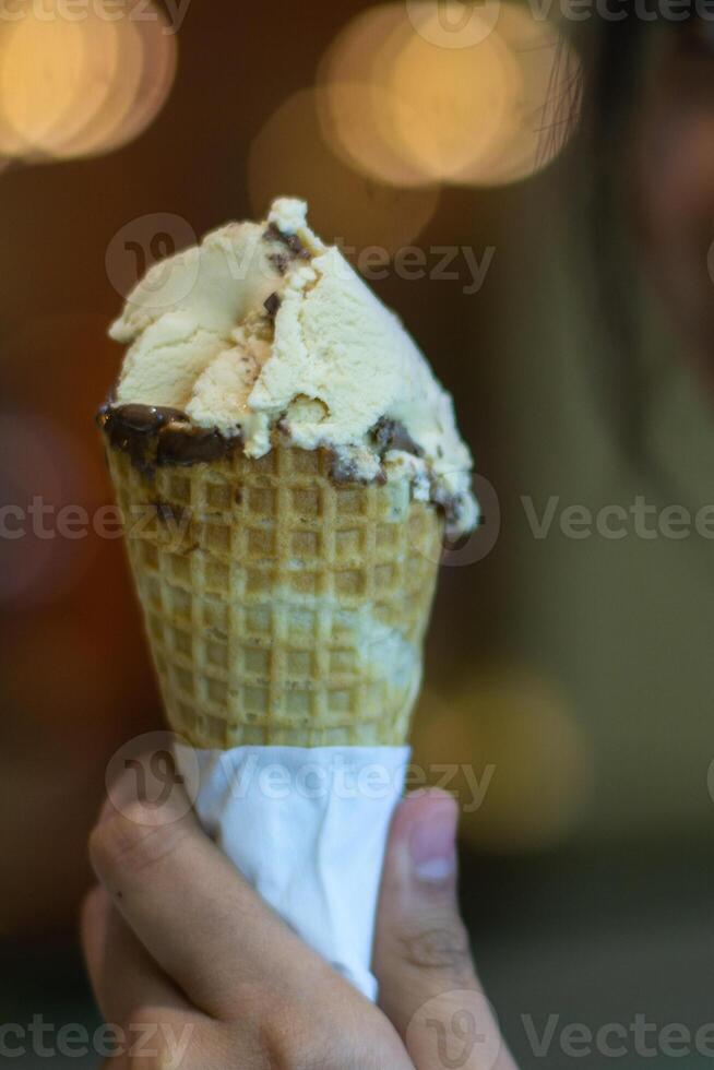 Close up hand of a person holding a cone of ice cream with blurred background photo