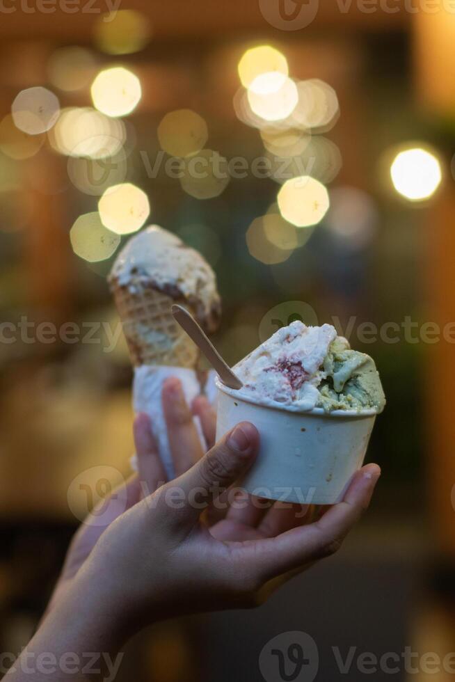Close up hand of a person holding a cup and a cone of ice cream with blurred background photo