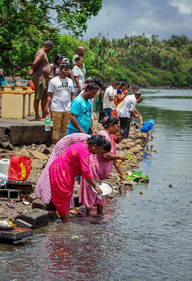 Port Louis, Mauritius - January 12, 2023 - A group of individuals, following Indian Hindu religious traditions, standing next to a body of water in Mauritius. photo
