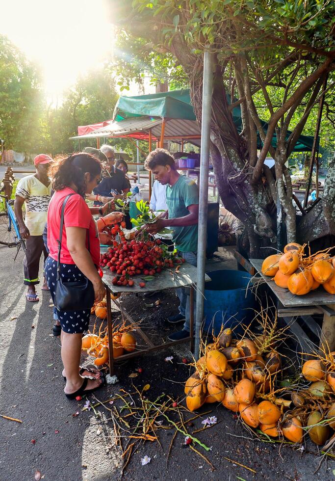 Port Louis, Mauritius - January 12, 2023 - A diverse group of individuals gather around a bustling fruit stand filled with an assortment of fresh lychees in Mauritius. photo