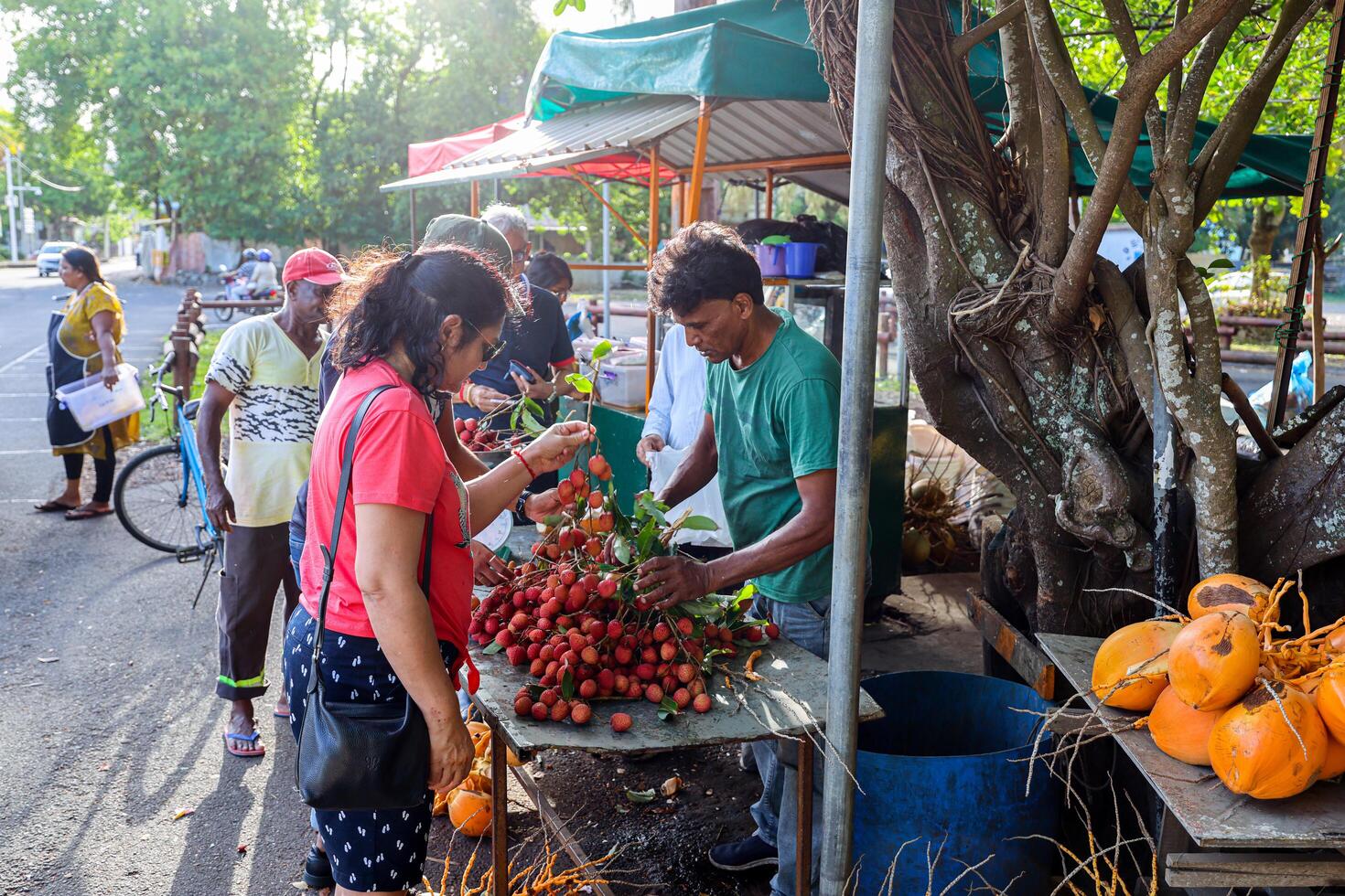 Port Louis, Mauritius - January 12, 2023 - A diverse group of individuals gather around a bustling fruit stand filled with an assortment of fresh lychees in Mauritius. photo