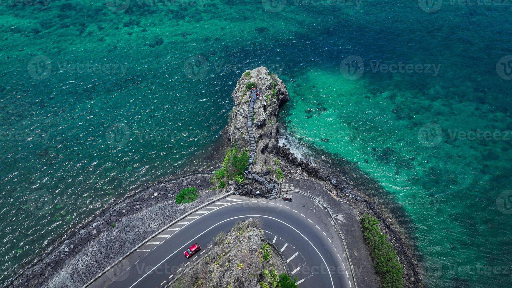 An aerial view captures a winding road as it travels towards the ocean, showcasing the interaction between man-made infrastructure and the natural environment. photo