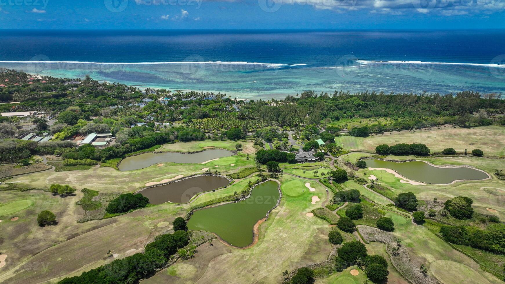 This aerial photograph showcases a golf course in Mauritius, with the fairways and greens beautifully laid out amidst a surrounding expanse of water. photo