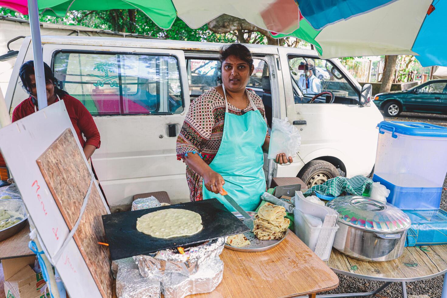 Port Louis, Mauritius - January 12, 2023 - A woman is seen preparing Indian food on a table under an umbrella, with a focus on making bread. photo