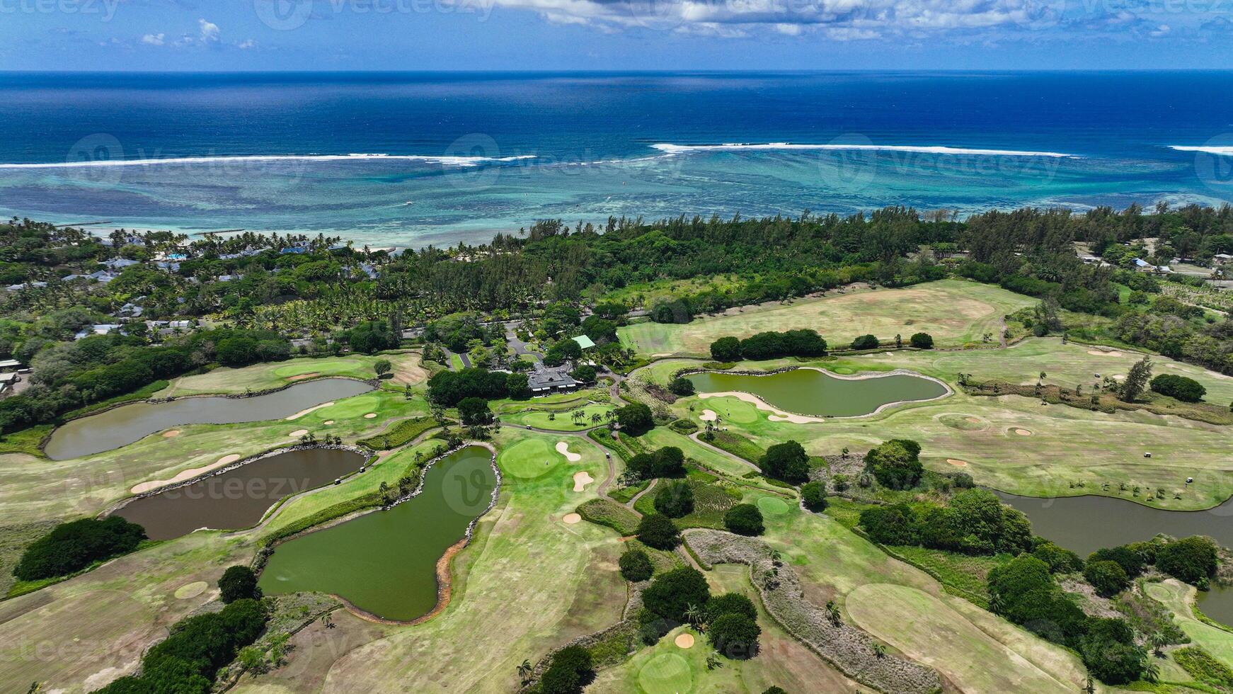 This aerial photograph showcases a golf course in Mauritius, with the fairways and greens beautifully laid out amidst a surrounding expanse of water. photo