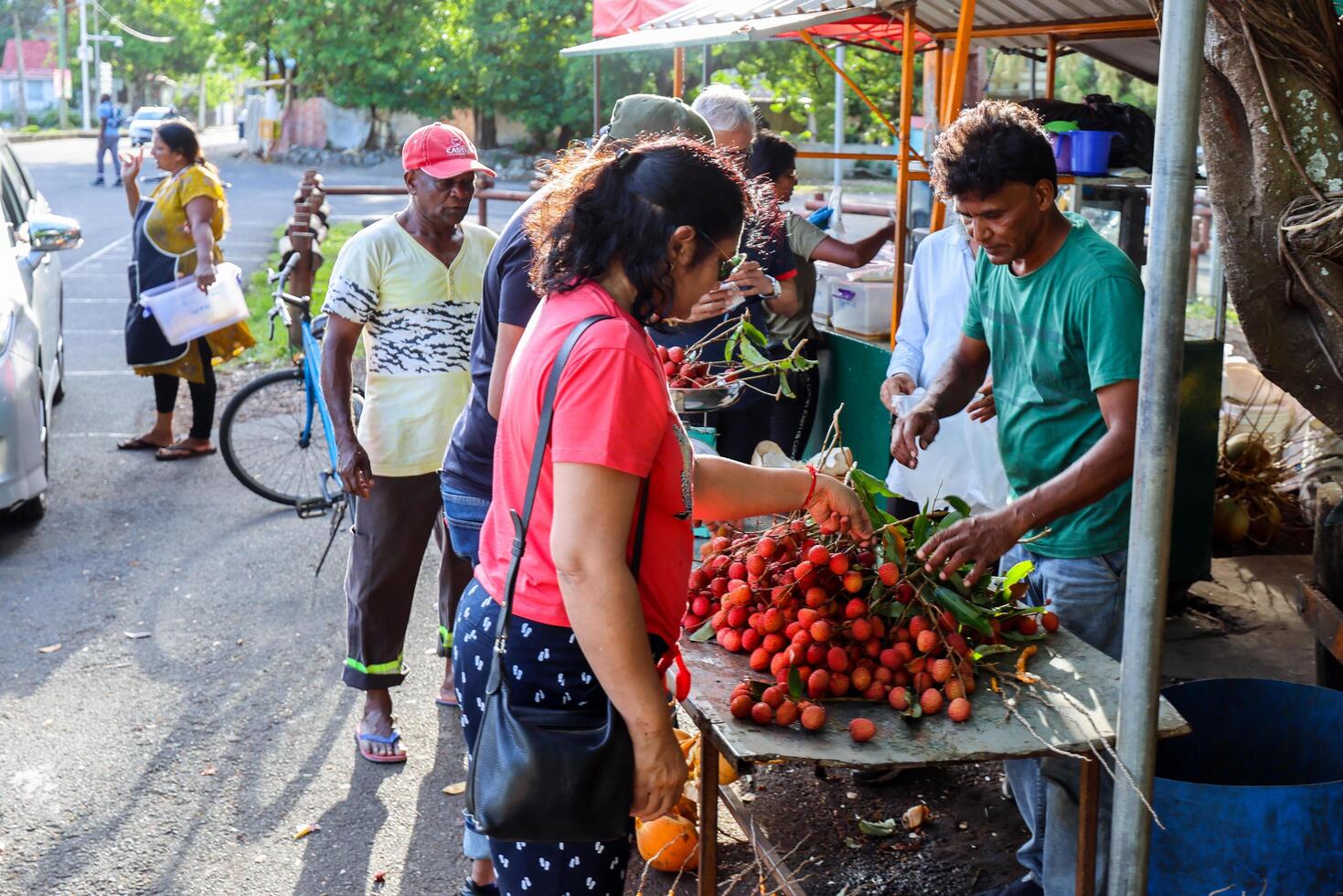 Port Louis, Mauritius - January 12, 2023 - A diverse group of individuals gather around a bustling fruit stand filled with an assortment of fresh lychees in Mauritius. photo