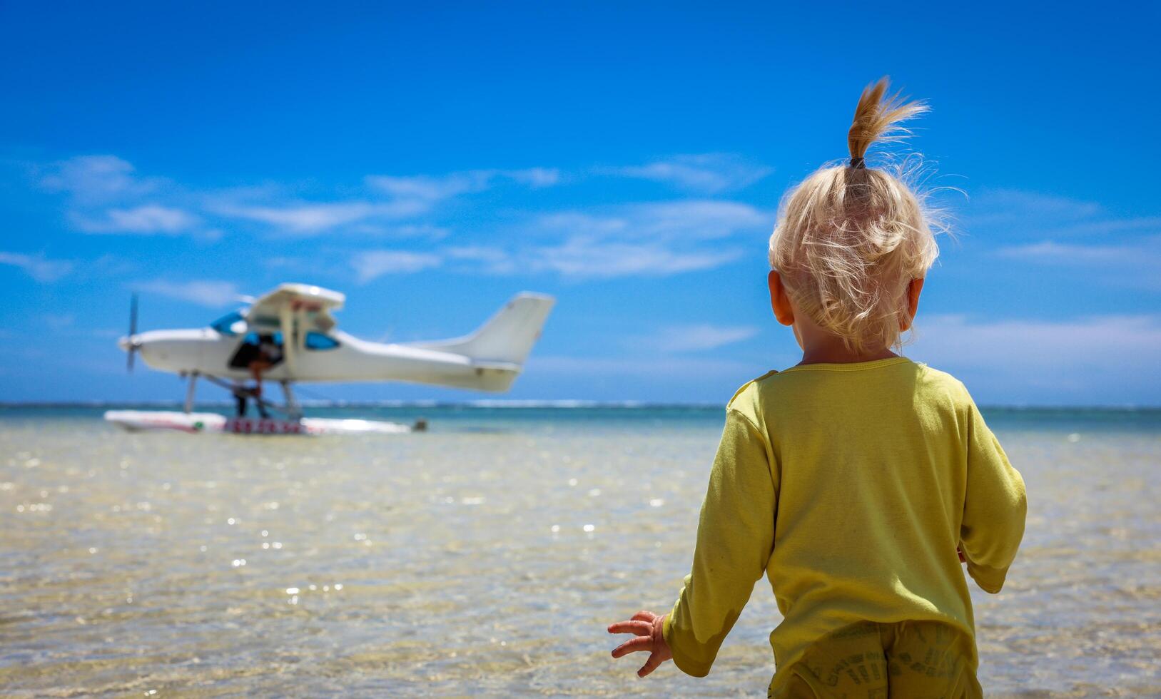 A little boy stands confidently in front of an airplane at the Mauritius beach photo