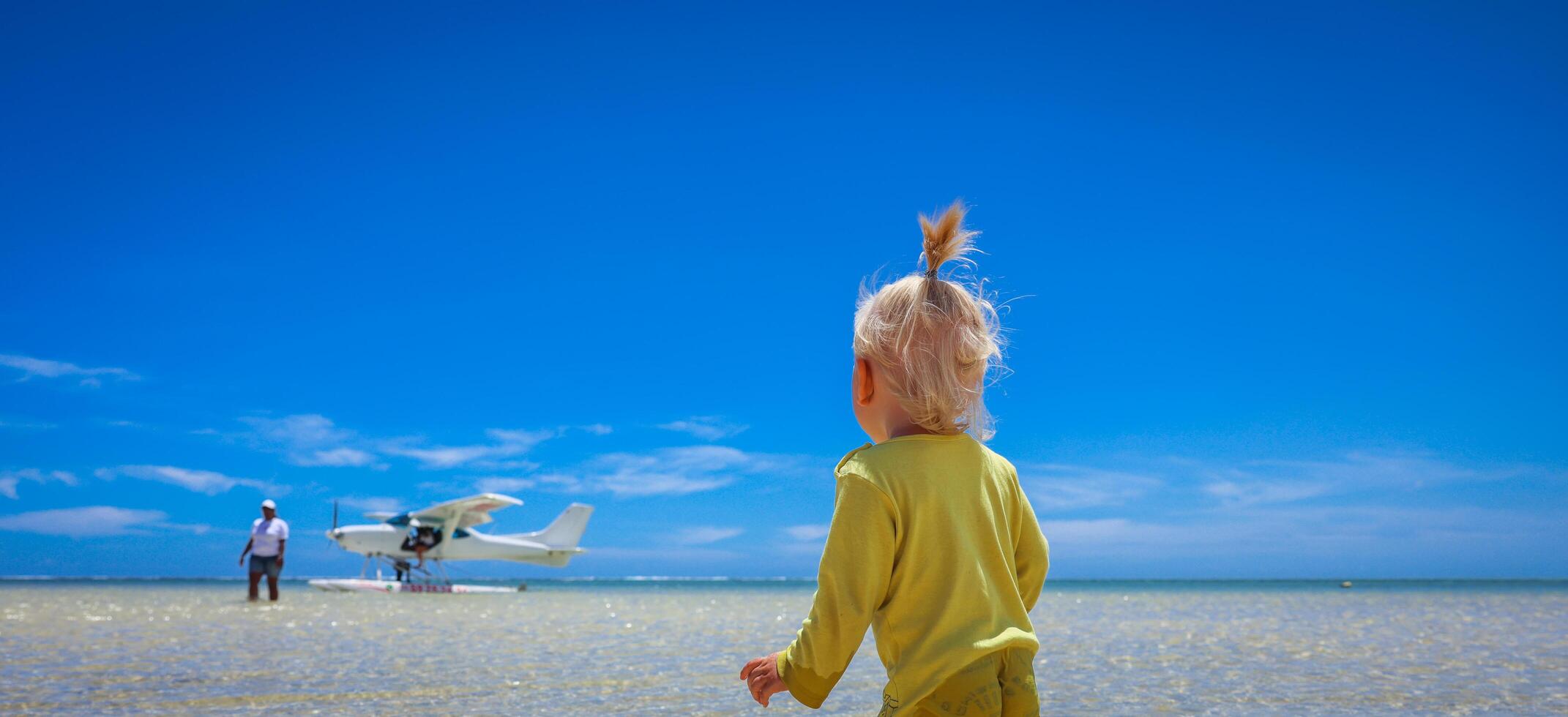 A little boy stands confidently in front of an airplane at the Mauritius beach photo