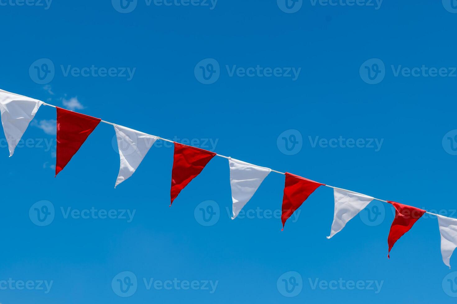 long line of flags with red and white stripes are hanging in the sky photo