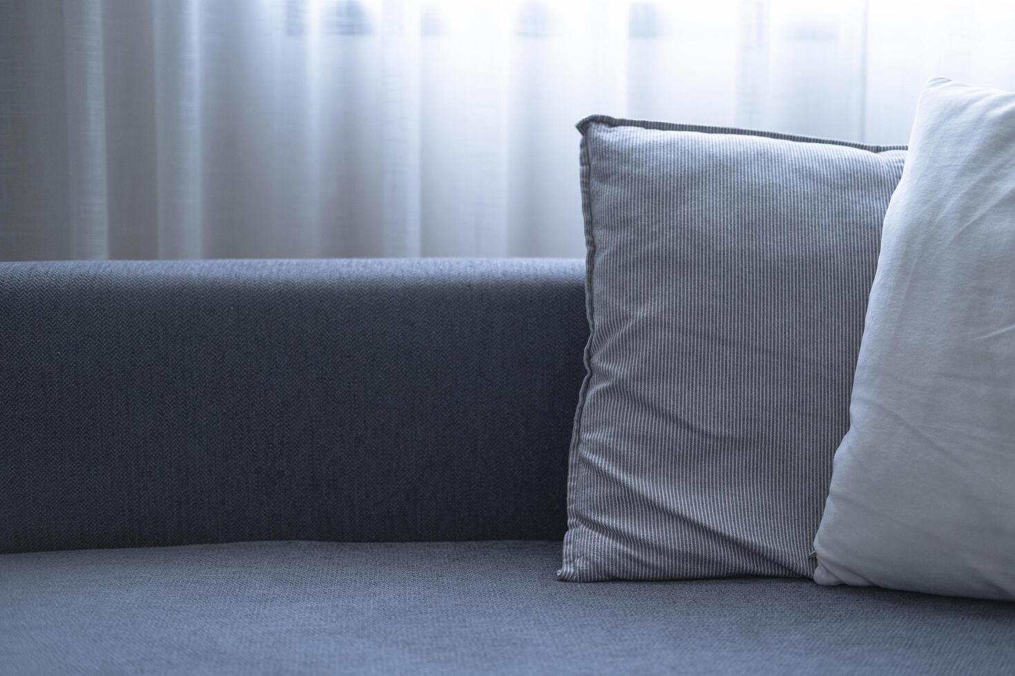 Close-up of cushions on cozy grey sofa. Modern interior of living room. with large window and sheer curtain. photo