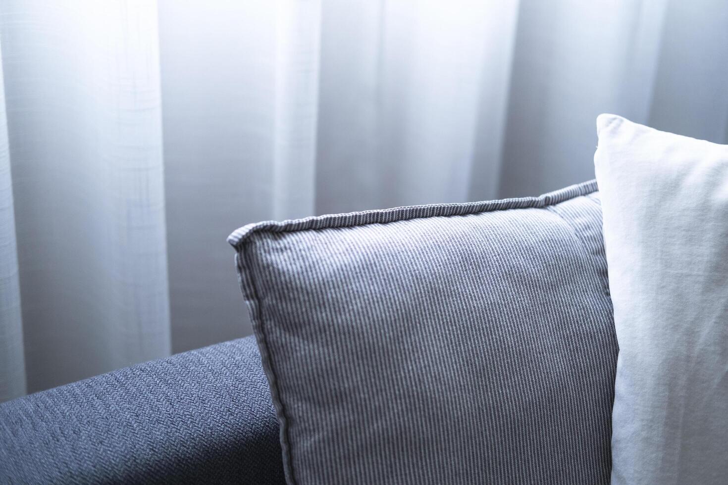 Close-up of cushions on cozy grey sofa. Modern interior of living room. with large window and sheer curtain. photo