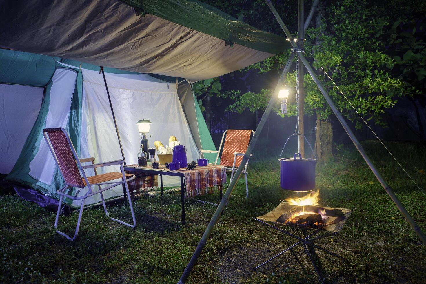 Camping tents at night, vintage cabin tents, Antique lanterns, retro chairs, and outdoor coffee-making facilities on wooden tables in a forest photo