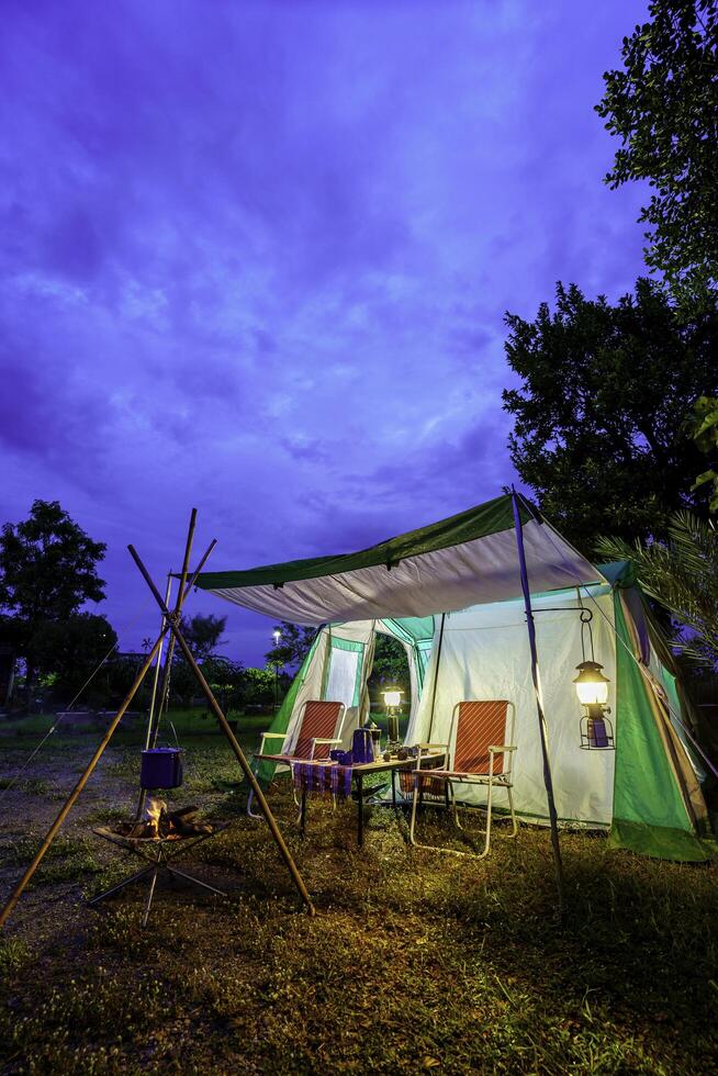 Camping tents at night, vintage cabin tents, Antique lanterns, retro chairs, and outdoor coffee-making facilities on wooden tables in a forest photo
