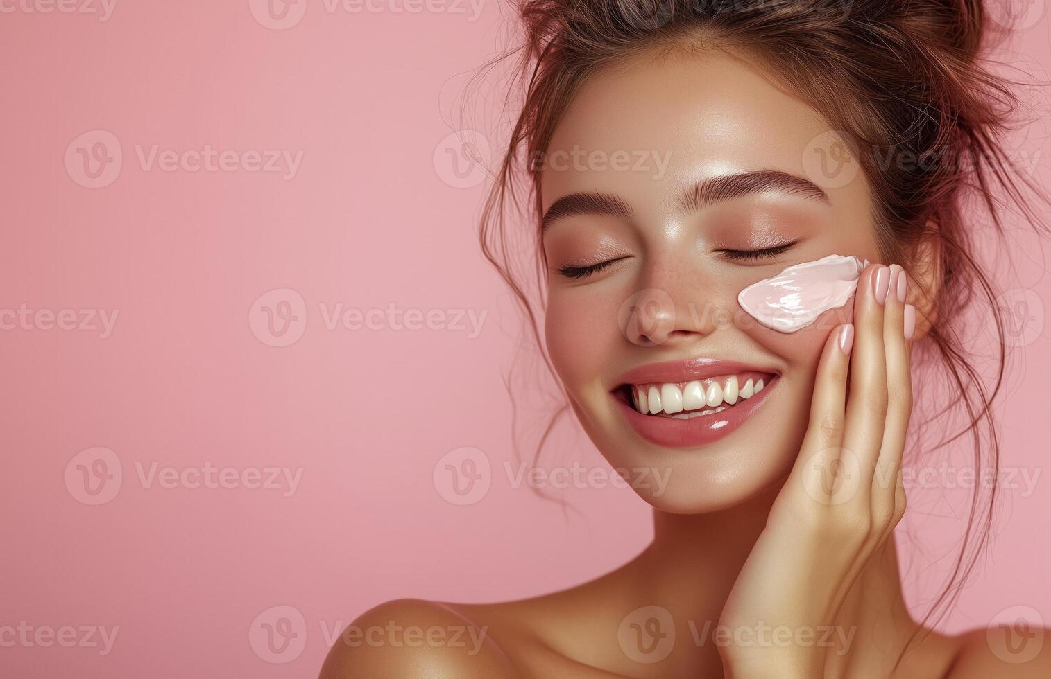 A lovely woman with closed eyes smiles while applying cream to her cheek with one hand photo
