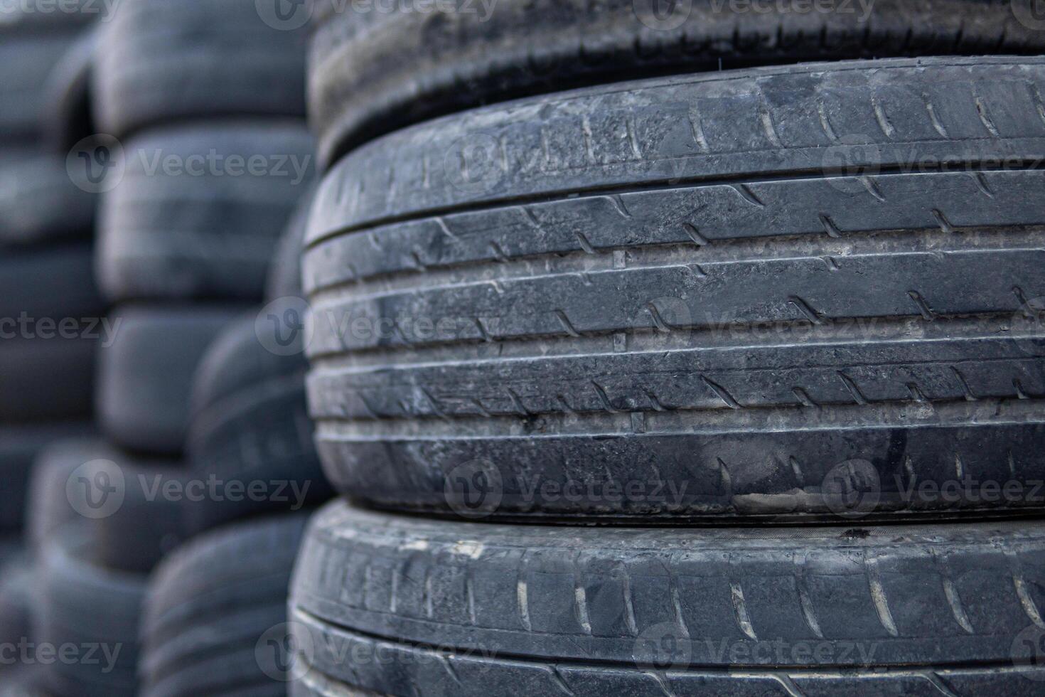 A pile of old tires stacked on top of each other. The tires are black and appear to be worn out. Concept of neglect and abandonment, as the tires are piled up and not being used. photo
