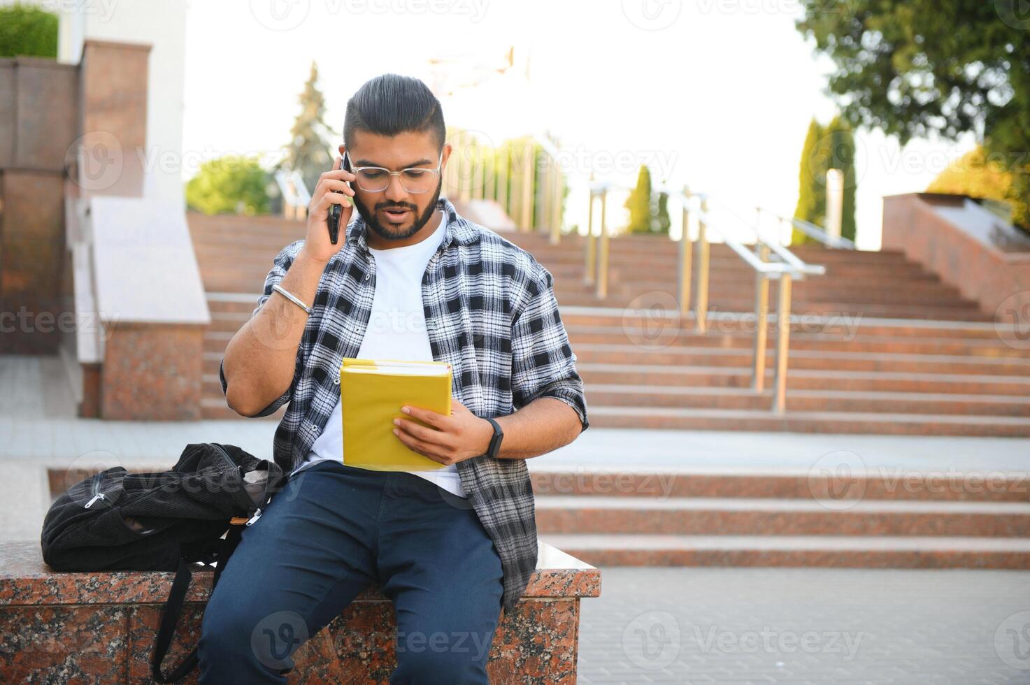 Young Indian male student using mobile phone, standing outside on street photo