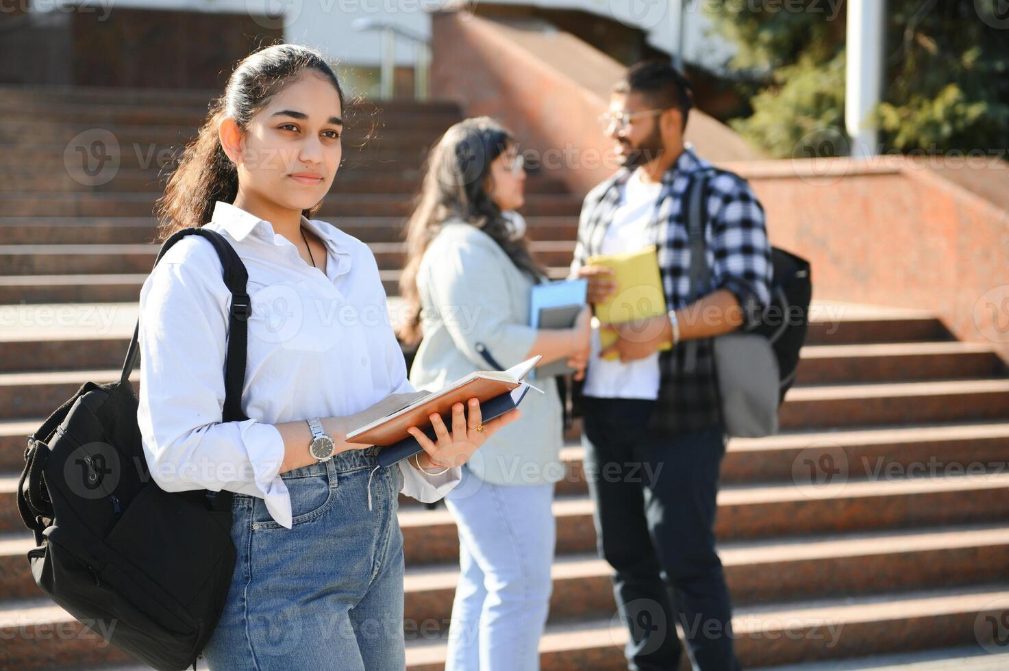 Three international students standing and holding a books photo