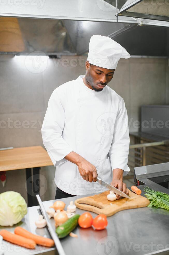 Experienced professional African-American chef standing in kitchen of restaurant with working staff photo