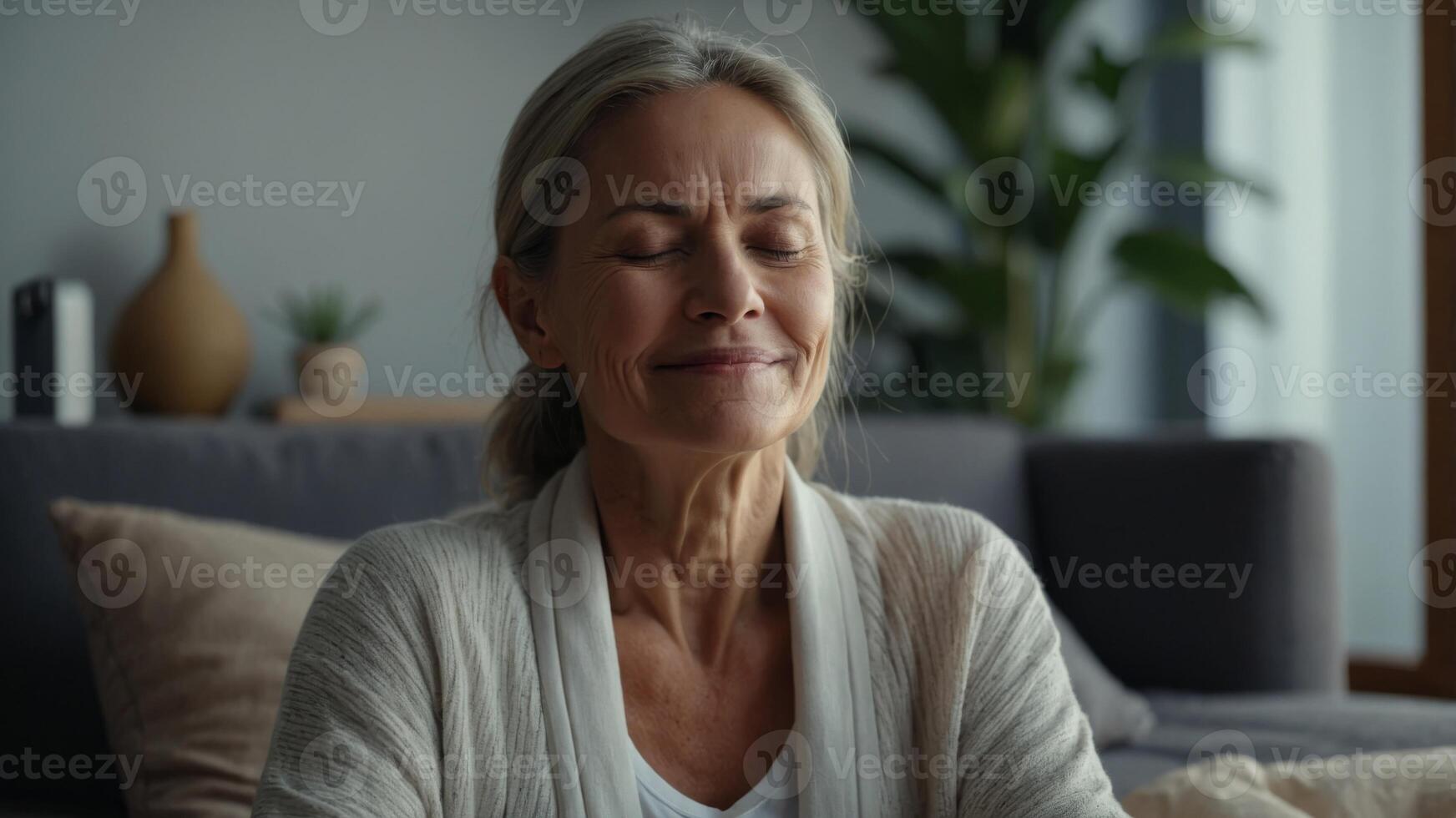 Positive serene beautiful mature lady enjoying calmness, relaxation, tranquility at home, posing with closed eyes and toothy smile, meditating, practicing stress relief, mindfulness techniques. photo
