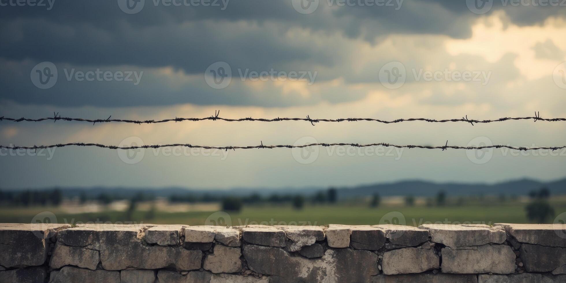 Barbed wire atop concrete wall under cloudy sky. photo