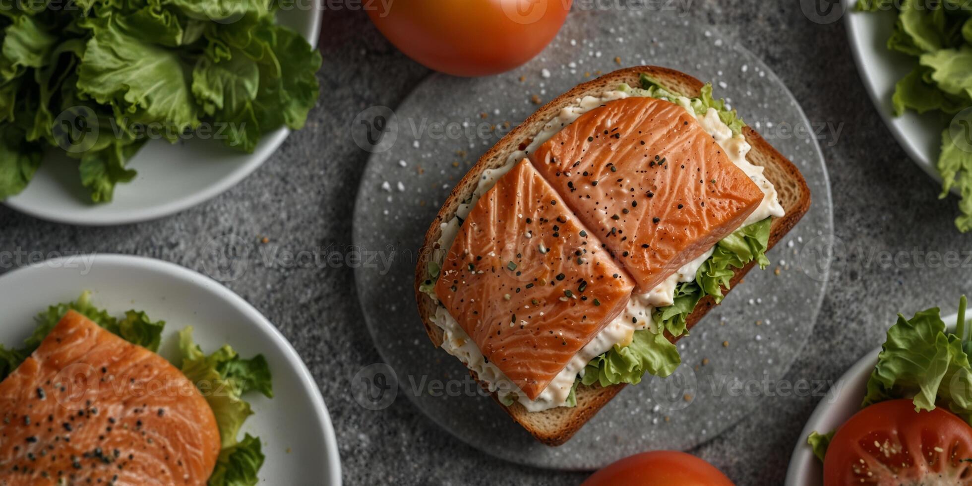 an overhead view of a salmon sandwich on a white plate with lettuce tomato and a gray speckled background. photo