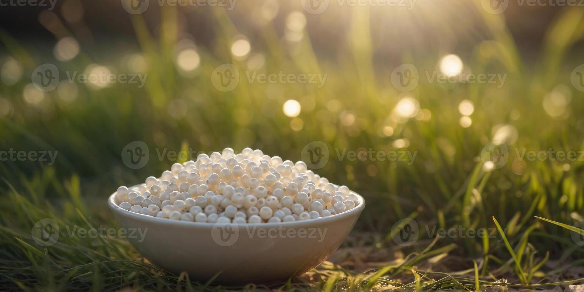 Bowl of white beads in grassy field under sunlight. photo
