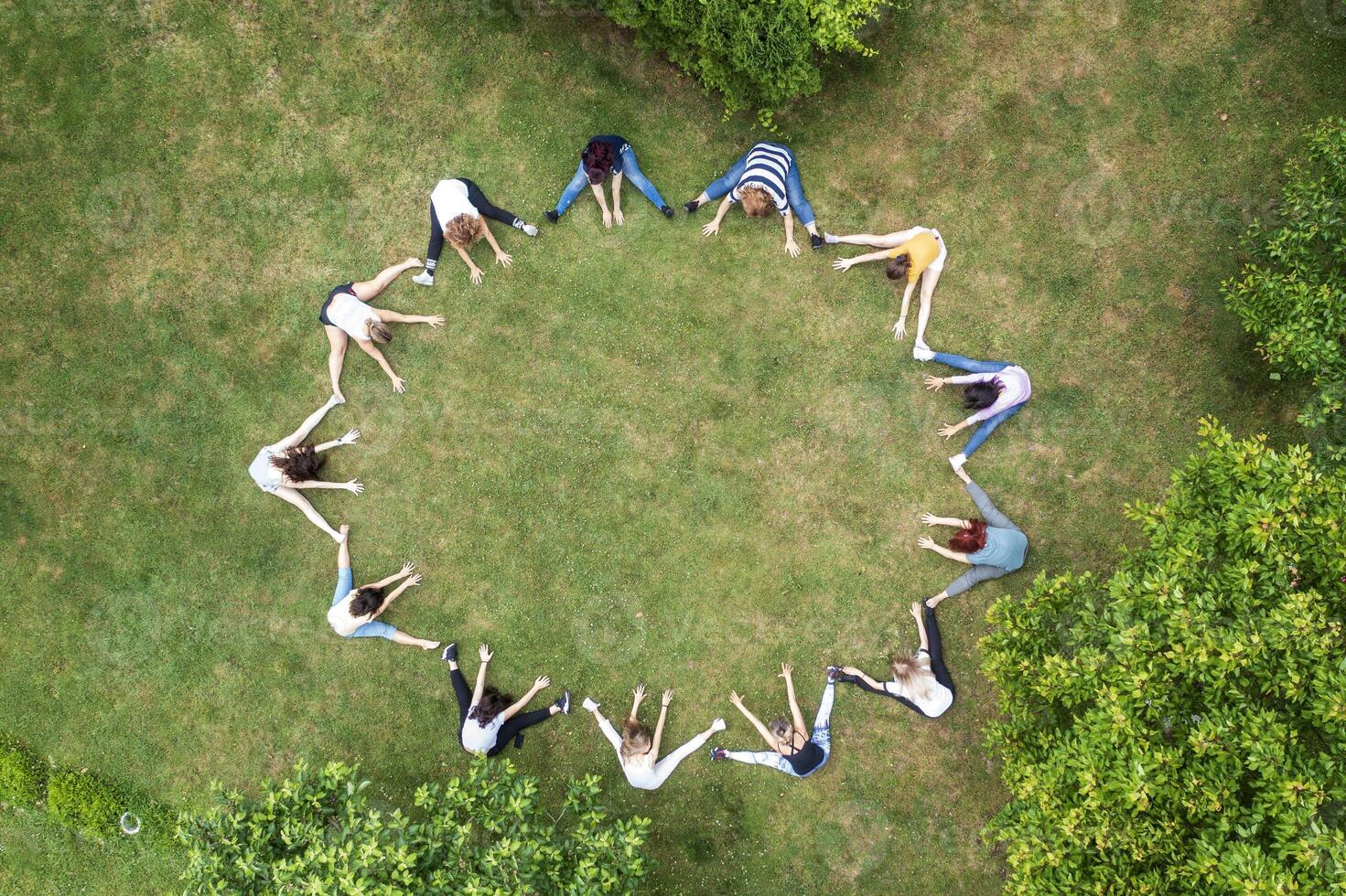 Top view of people standing in circle on green grass doing exercises photo
