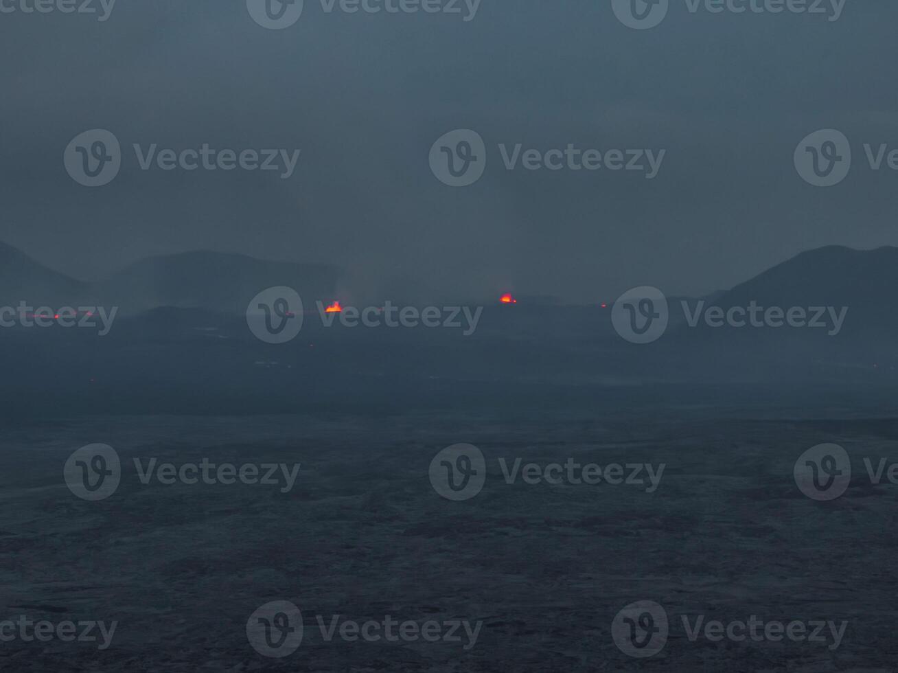 Aerial view of a dark, misty volcanic landscape in Iceland, featuring small glowing red volcanic vents in the distance. Captivating and mysterious scenery. photo