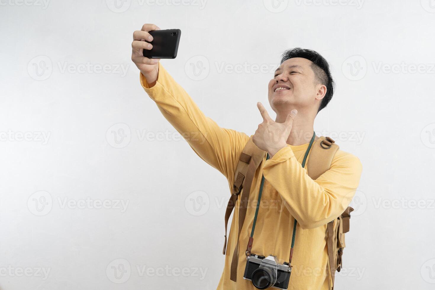 Smiling attractive young tourist with backpack walking and taking selfie mobile phone on white background. Passenger traveling on weekends. photo