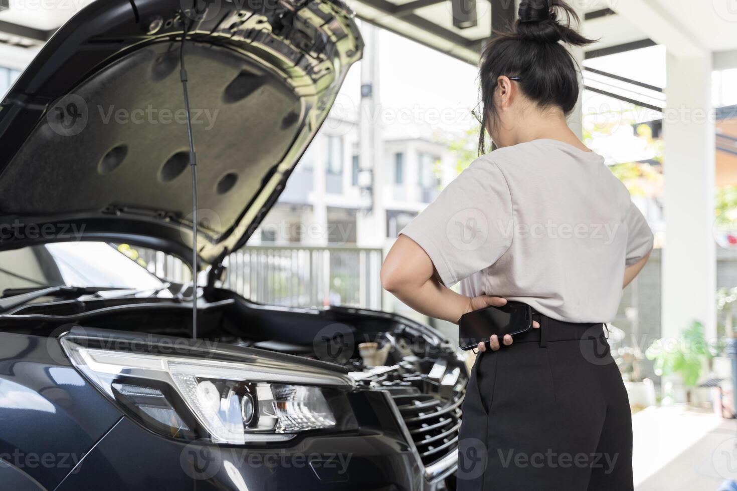 Young woman using mobile phone while looking at broken down car. photo