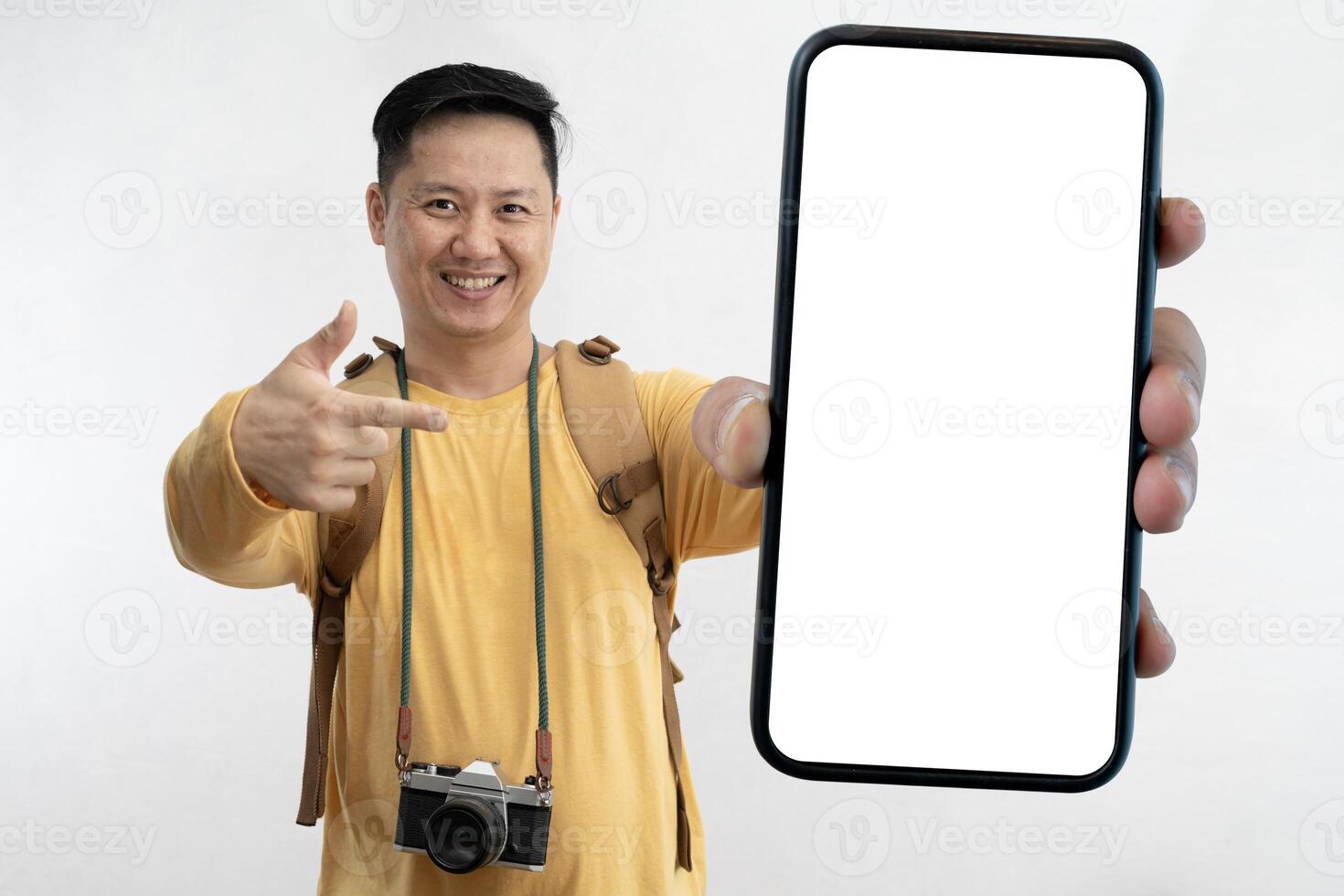 Excited tourist traveling with camera backpack and showing large empty smartphone at camera. Happy male traveler having fun against gray background. photo