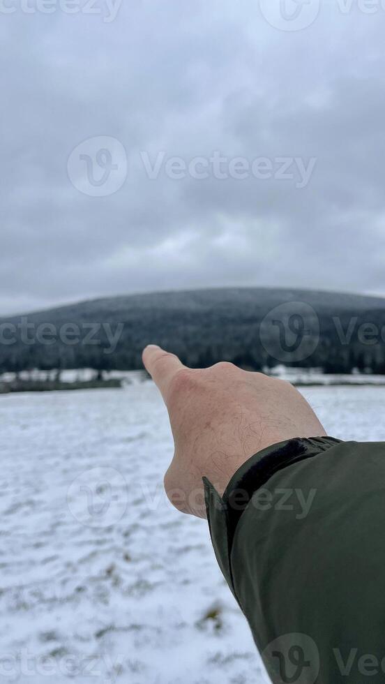 A finger of a hand points to a mountain peak in winter. photo