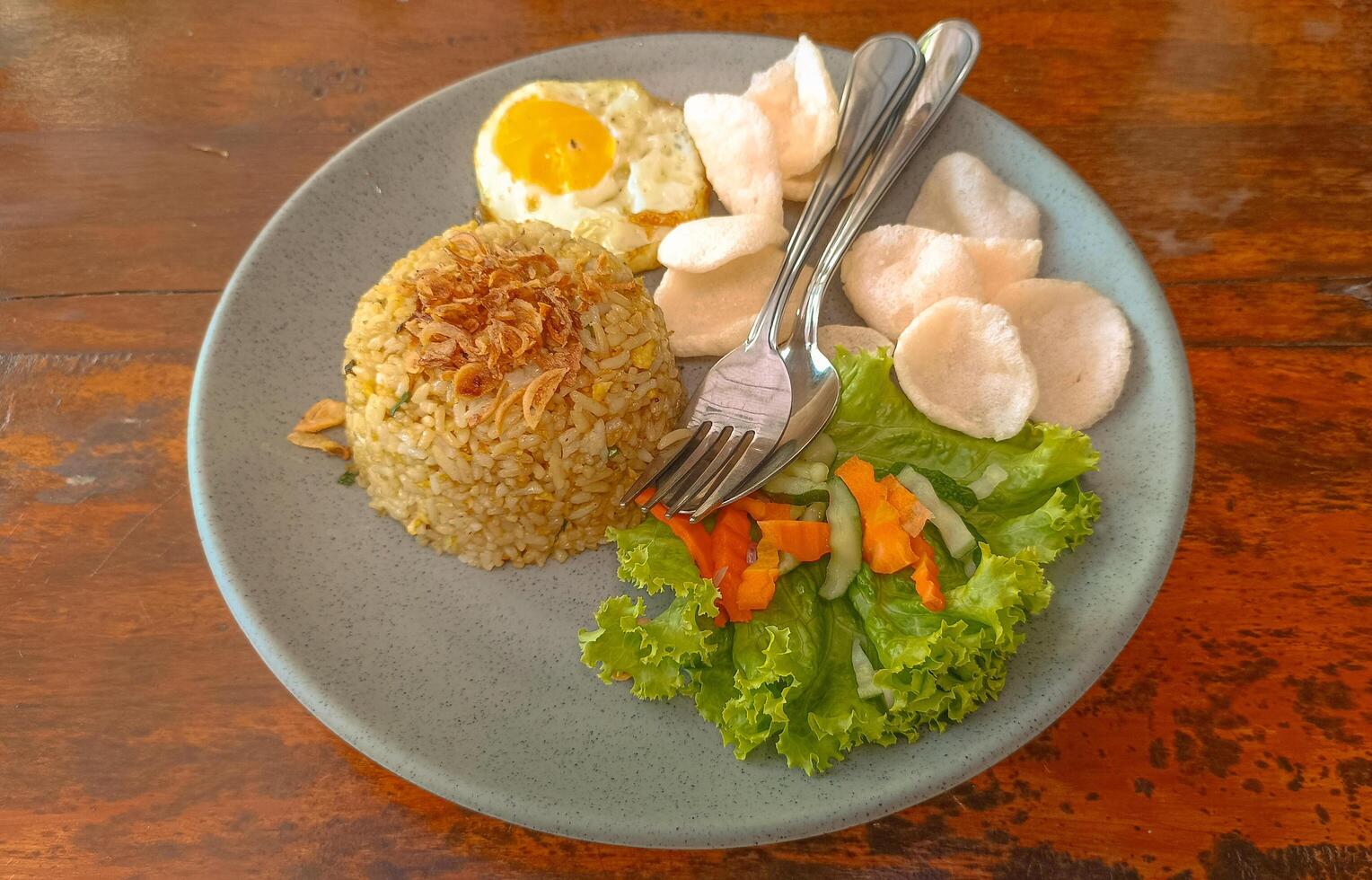 Indonesian fried rice with vegetables, fried egg and crackers in blue plate on wooden background photo