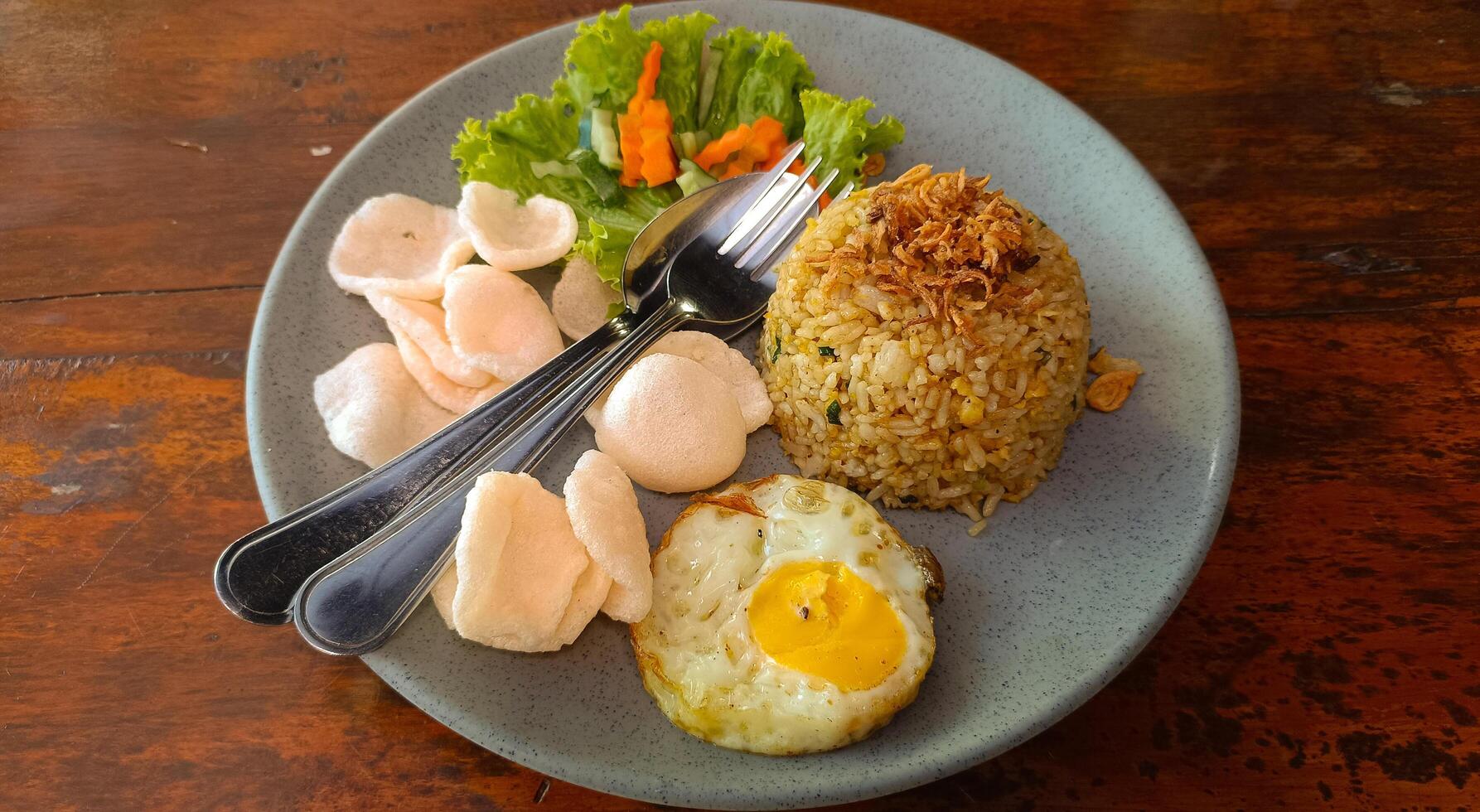 Indonesian fried rice with vegetables, fried egg and crackers in blue plate on wooden background photo