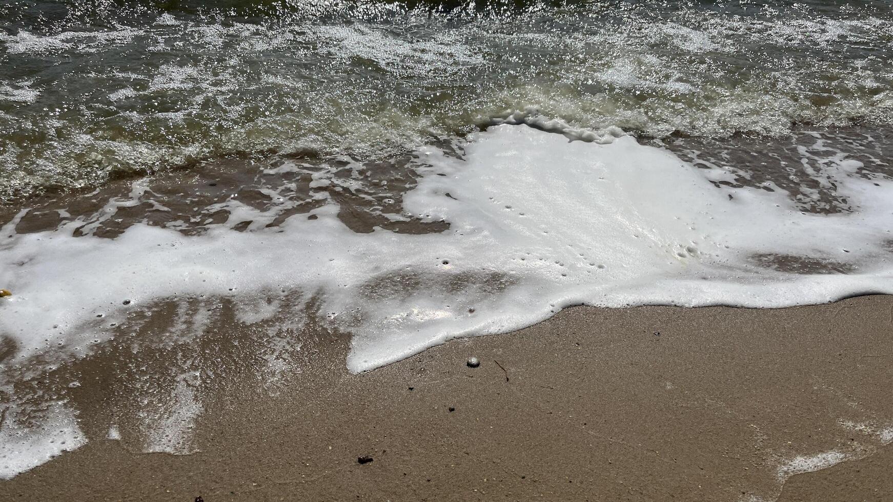 Nature photo of foamy beach waves. Soft wave on sand beach, text copy space for banners, cards. Close up of sea blue waves break on sand