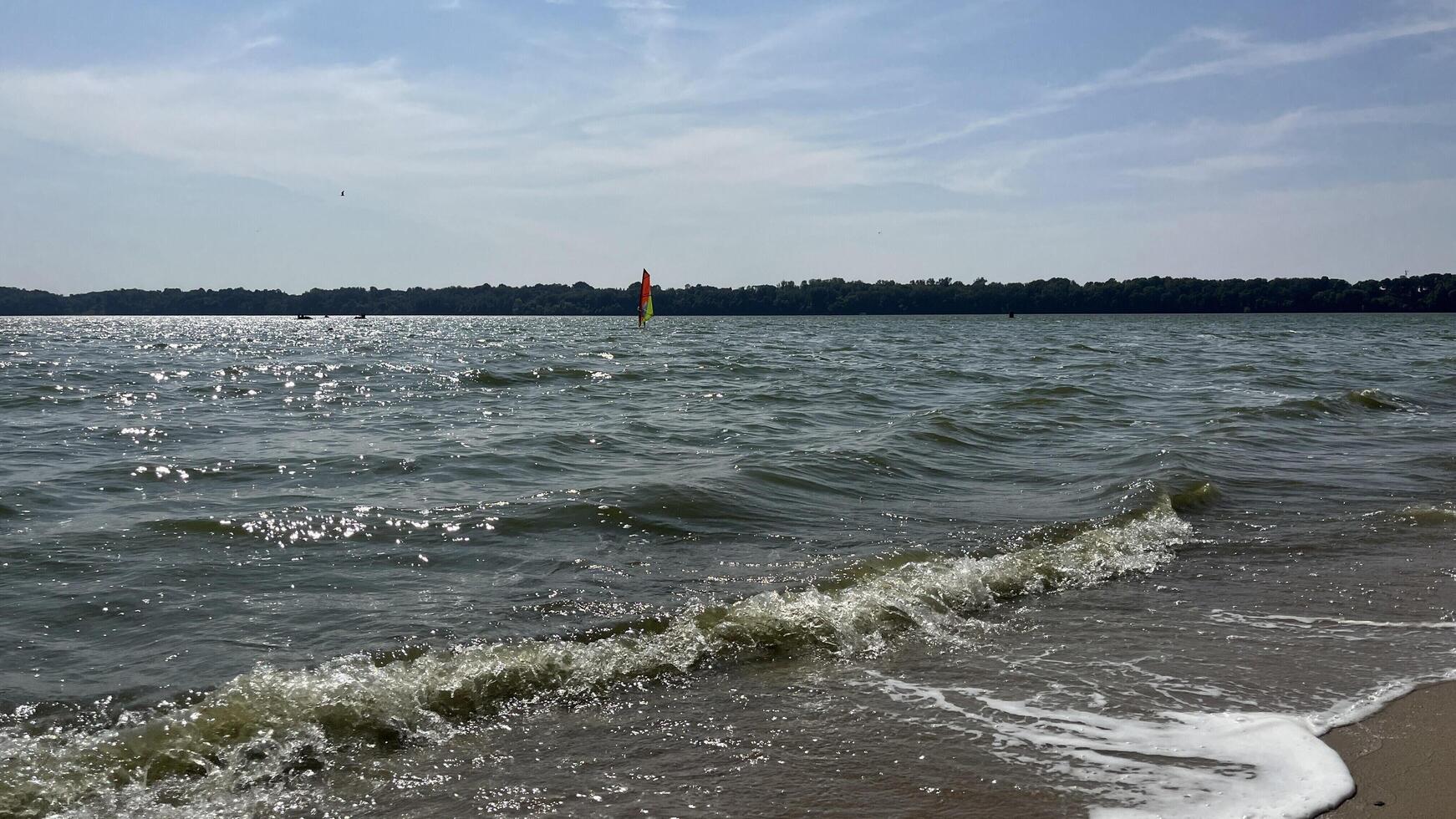 Nature photo of soft beach waves with unrecognize people sailing in beach. Text copy space for banners, cards.