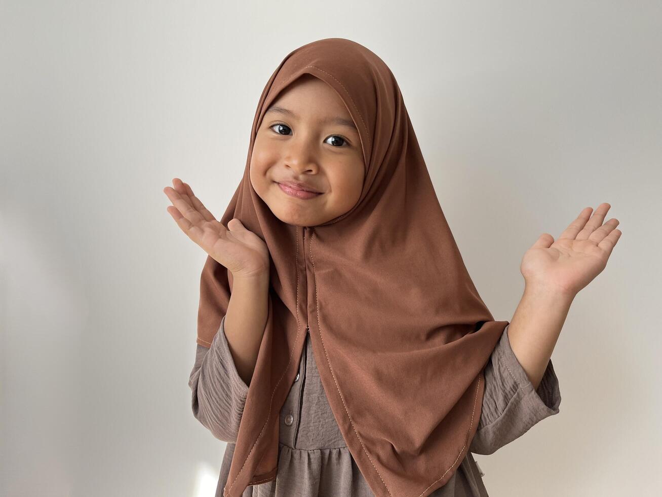 Asian Muslim little girl wearing hijab smiling showing gesture with both hand rising photo