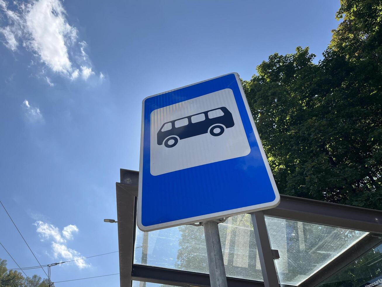 Bus stop sign with bus stop roof, leaves and blue sky in the background photo