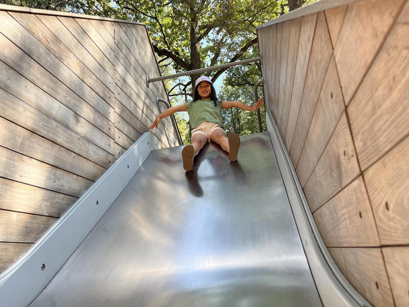 A little Asian girl is happily playing on the slide in playground. Bottom view photo