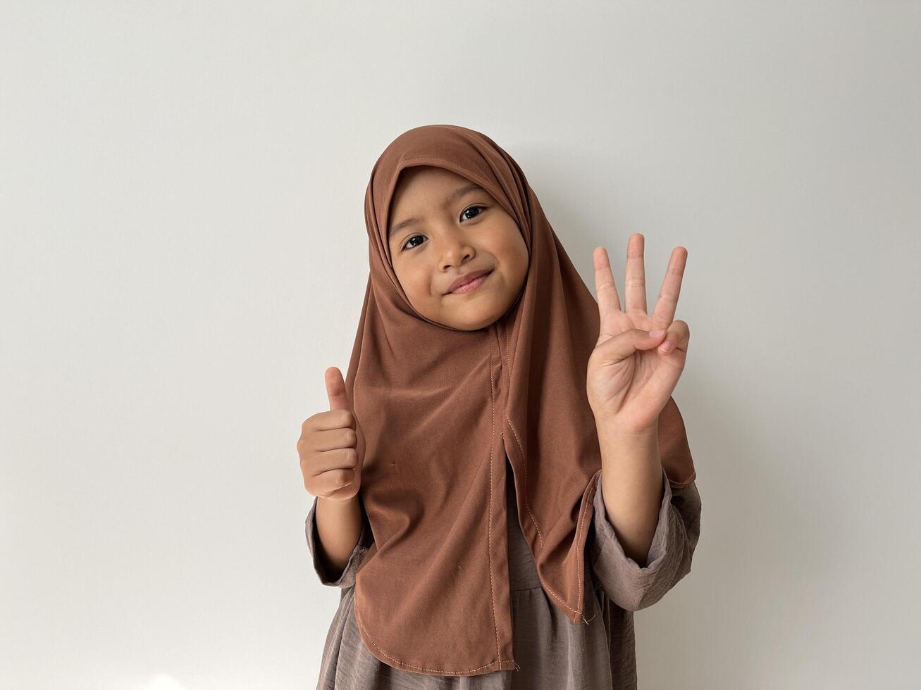 Asian Muslim little girl wearing hijab smiling at the camera show thumbs up gesture. photo