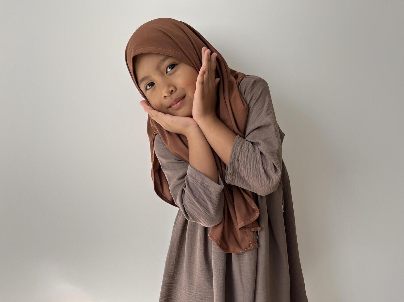 Asian Muslim little girl wearing hijab show cute face with both hands are on the chin photo