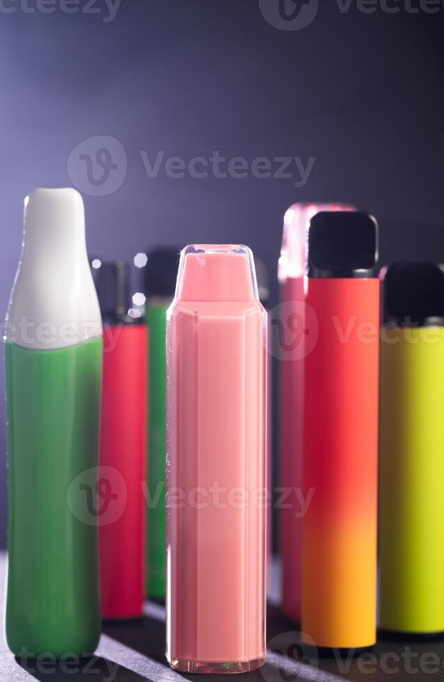 A set of colorful disposable electronic cigarettes of different shapes on a black background with smoke. Concept of modern smoking, vaping and nicotine. photo