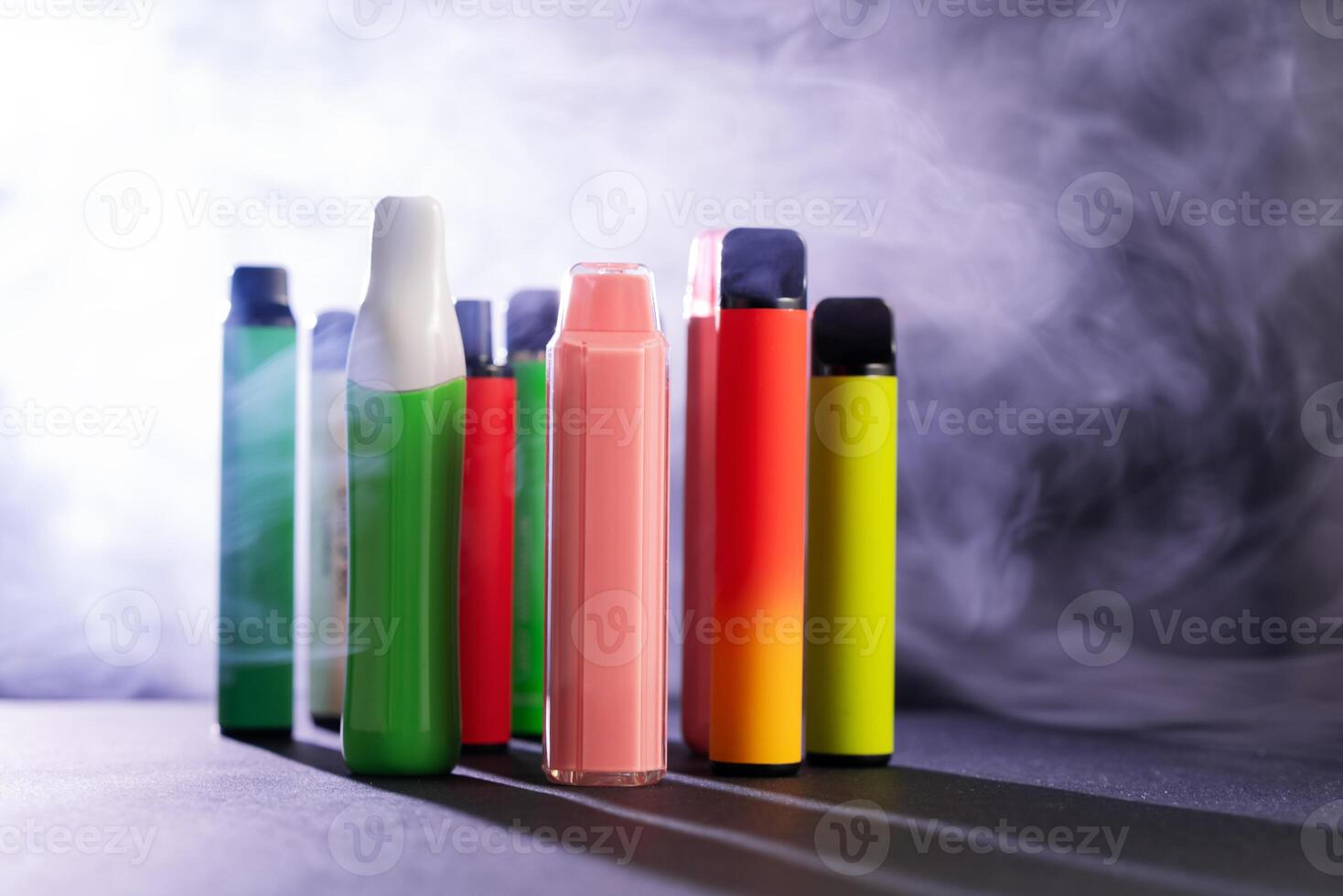 A set of colorful disposable electronic cigarettes of different shapes on a black background with smoke. Concept of modern smoking, vaping and nicotine. photo
