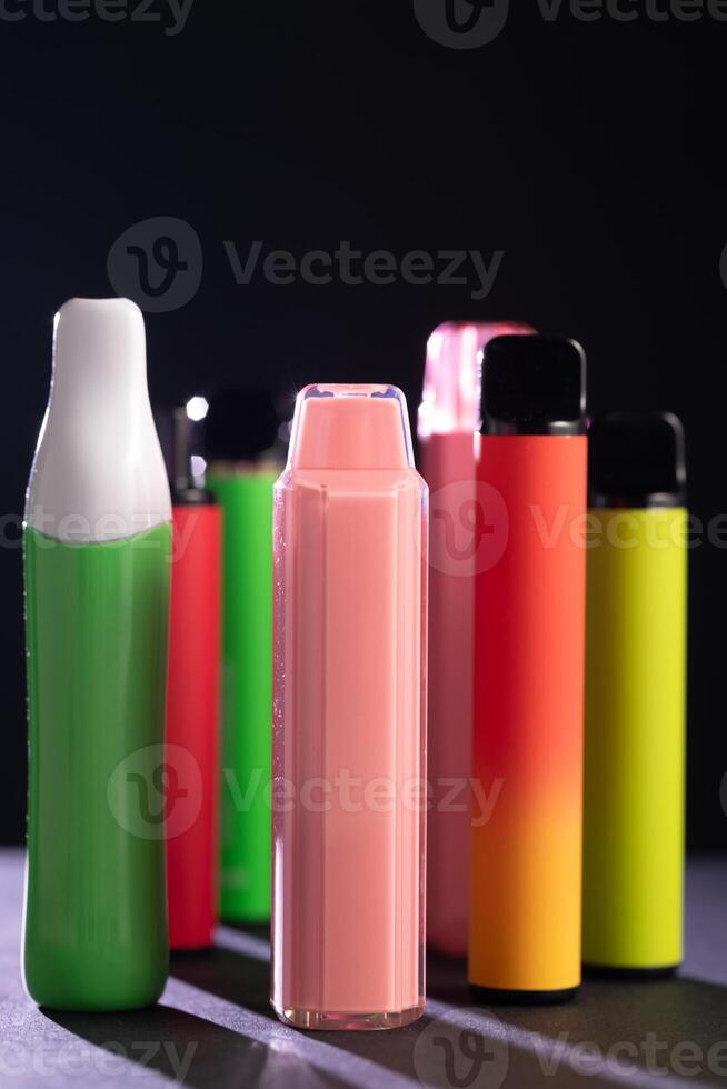 A set of colorful disposable electronic cigarettes of different shapes on a black background with smoke. Concept of modern smoking, vaping and nicotine. photo